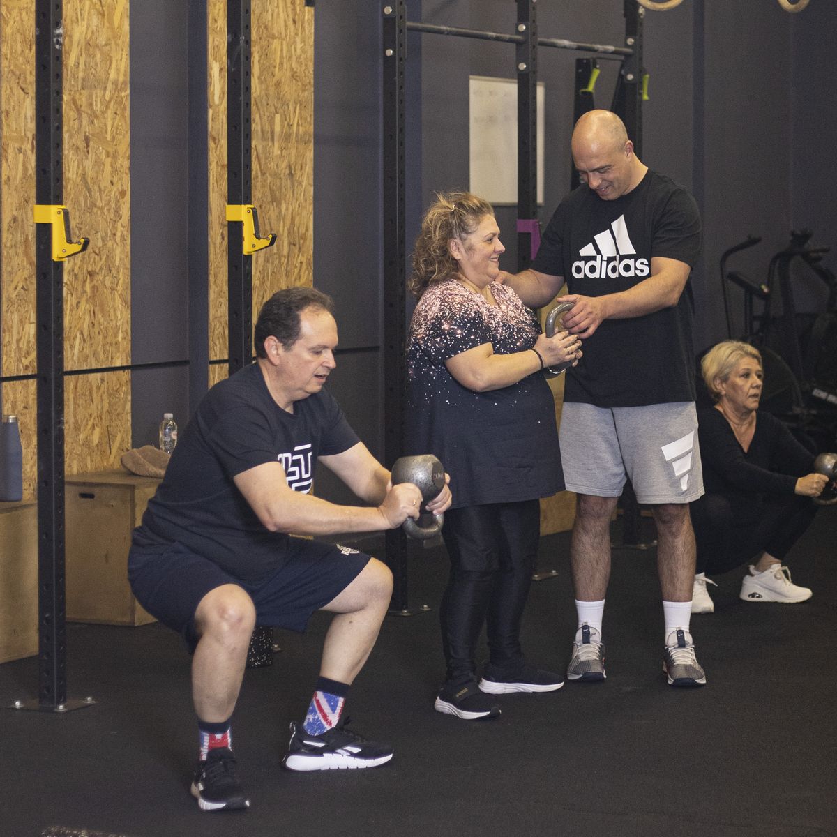 Μικρή ομάδα στη LIFT κάνει καθίσματα με kettlebell, ενώ ο προπονητής βοηθά μια αθλούμενη.
